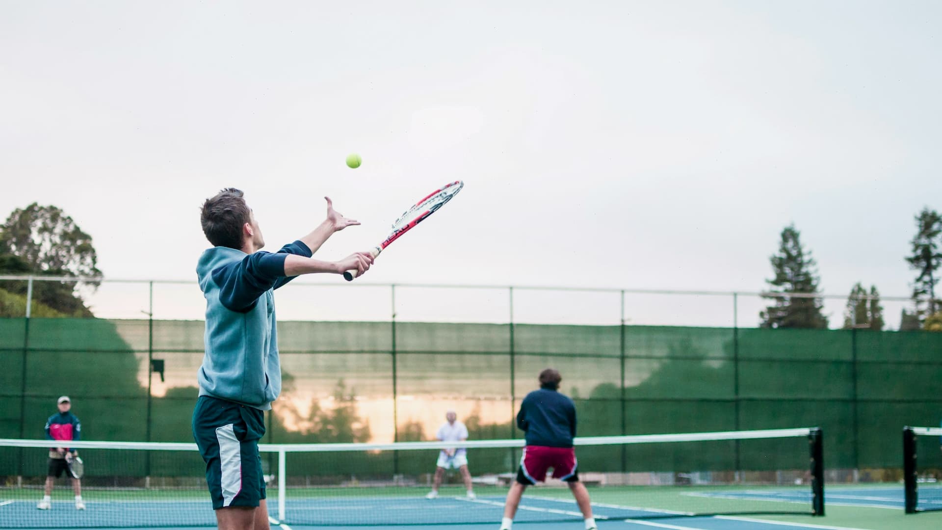 Jugador de tenis sacando la pelota en la cancha con otros jugadores al fondo